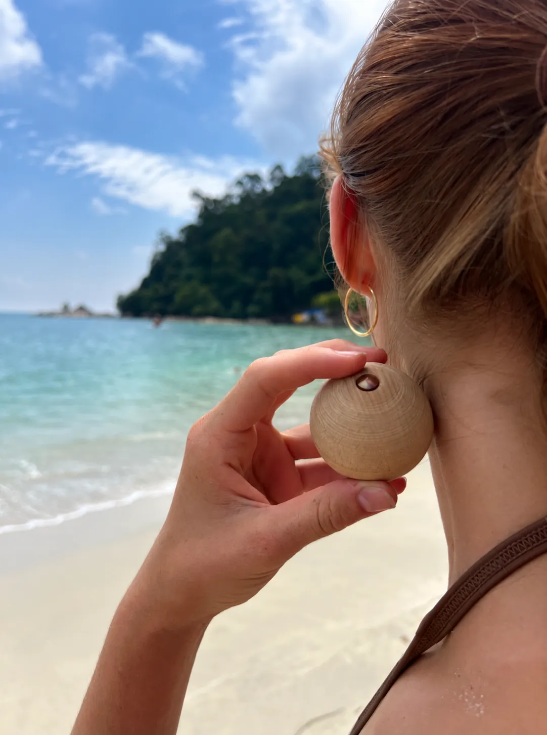 A woman on the beach holding the ball against the side of her neck below the ear