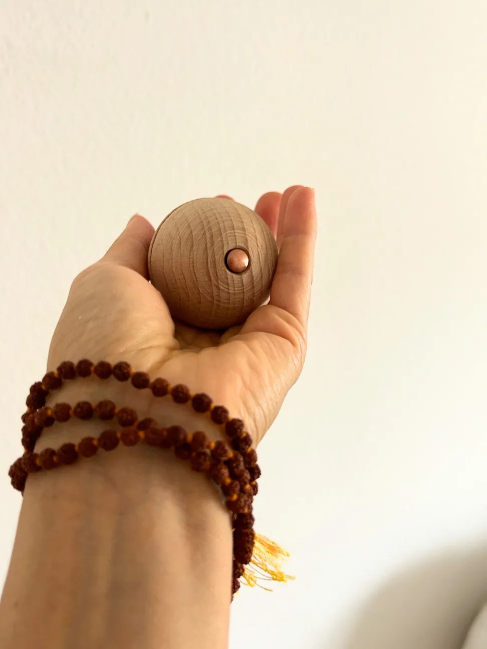 A hand open and upward, holding the ball, a wooden bead bracelet on the wrist