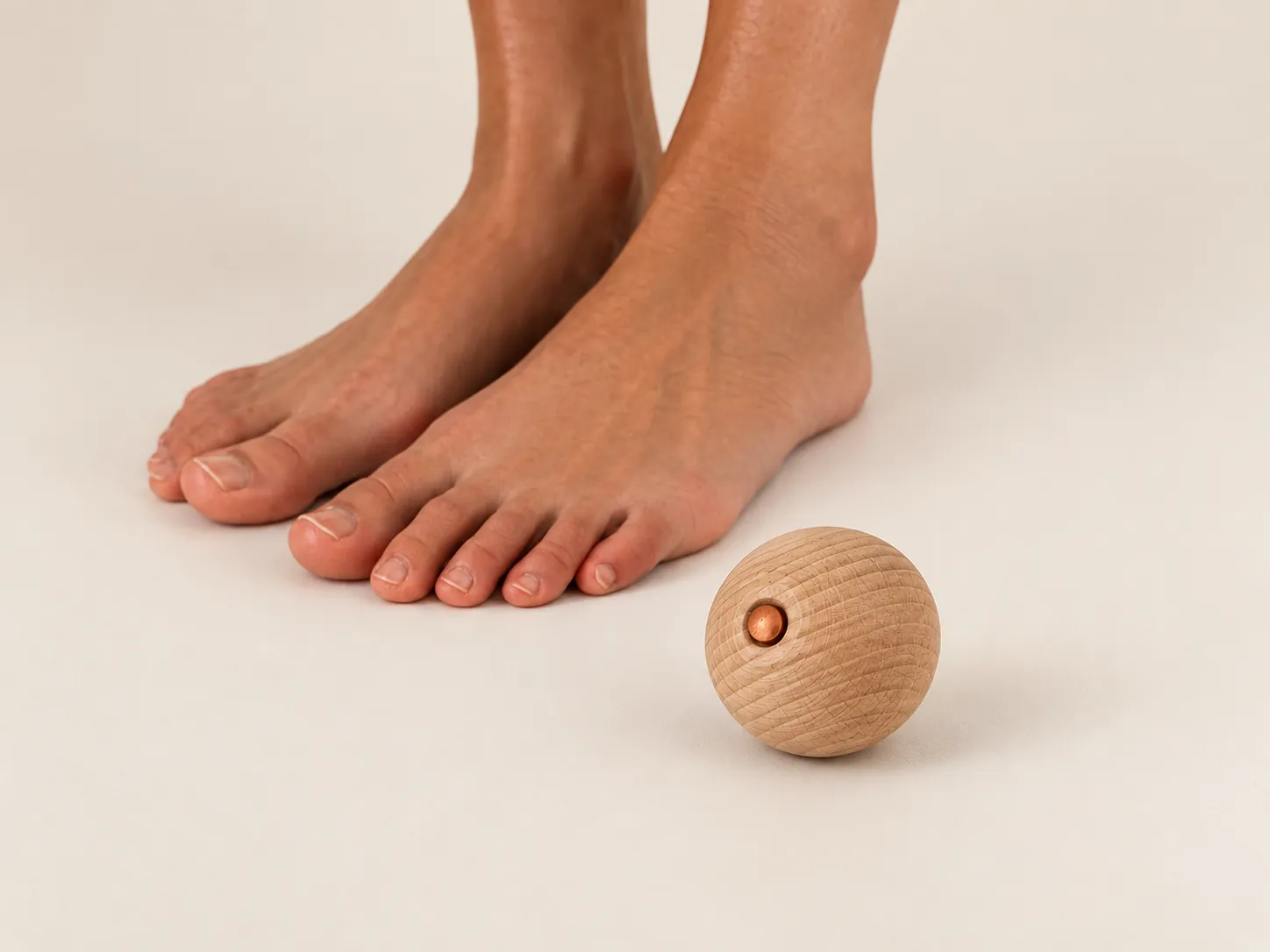 Bare feet on a cream floor beside the beech wood ball with its copper core